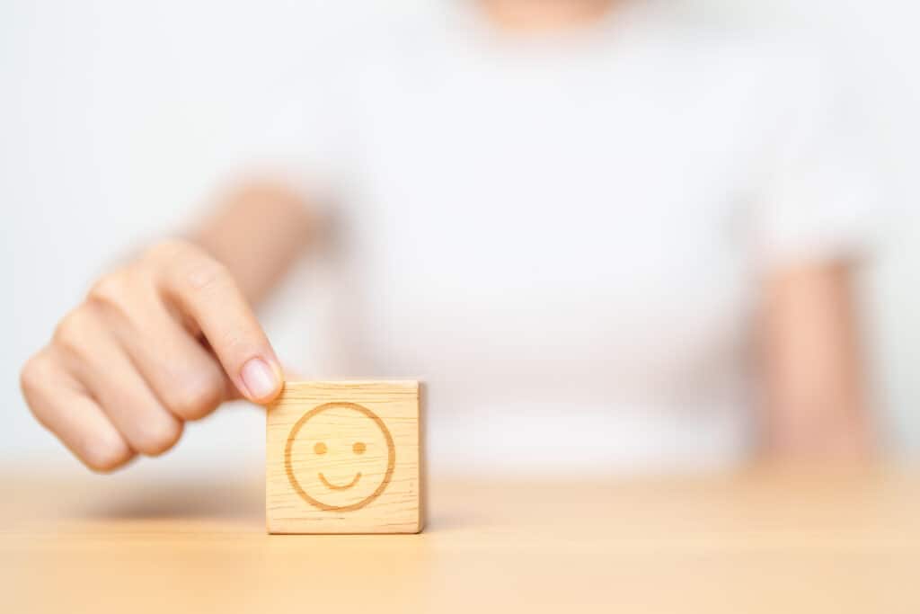 Hand choosing happy face from Emotion block for customer review, good experience, positive feedback, satisfaction, survey, evaluation, assessment, mood and world mental health day concept